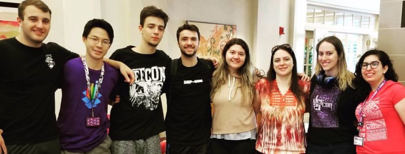 A photo of Kaitlyn Bestenheider posing with a group of seven other people in attendance at DEF CON.